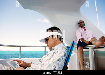 Man using tablet while sitting by friend on yacht Stock Photo