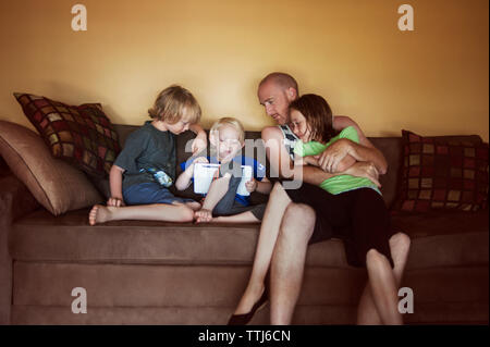 Family using tablet computer while sitting on sofa at home Stock Photo