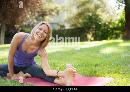 Portrait of woman touching toes while exercising on field Stock Photo
