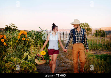 Couple holding hands while walking in farm against clear sky Stock Photo