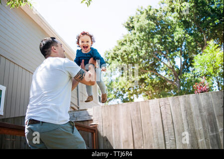 Low angle view of father lifting daughter while standing in backyard Stock Photo