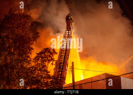 Rear view of firefighter spraying water on burning building Stock Photo