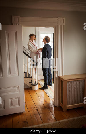 Woman holding man's tie while standing on staircase at home Stock Photo