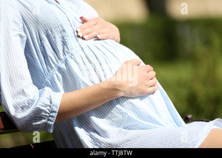 Pregnant woman sitting on chair in park Stock Photo
