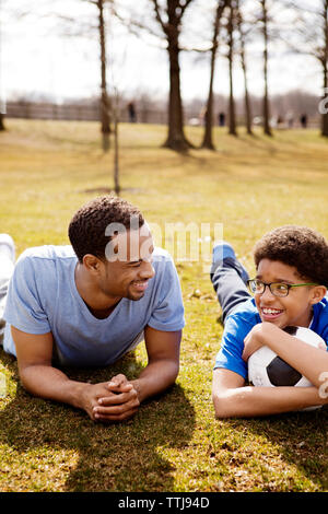 Father and son with soccer ball lying on field in park Stock Photo