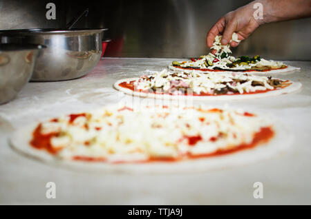 Cropped image of hand putting cheese on pizza Stock Photo
