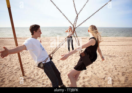 Woman photographing friends on swing at beach Stock Photo