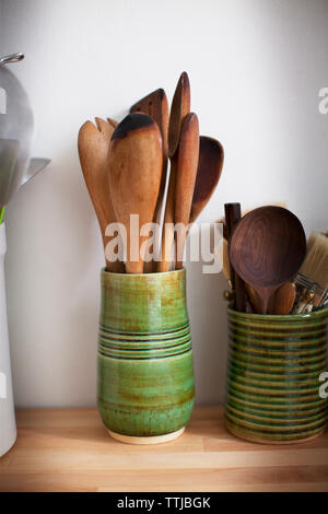 Wooden spoons in container on table against wall at home Stock Photo