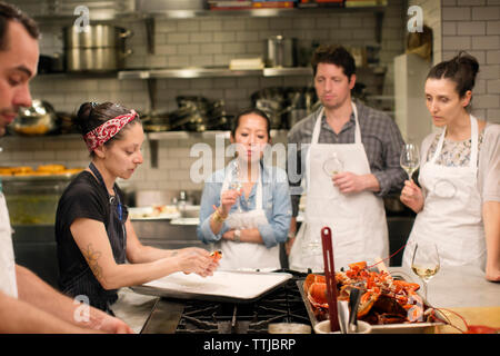 Students looking at female chef preparing food at commercial kitchen Stock Photo