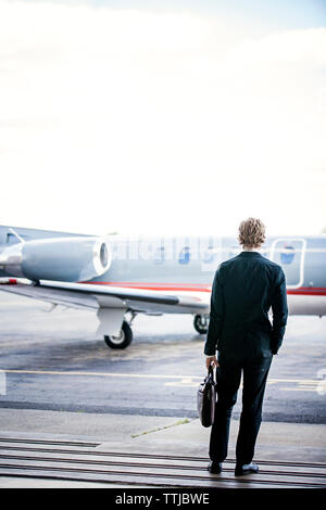 Rear view of businessman standing by airplane against clear sky Stock Photo