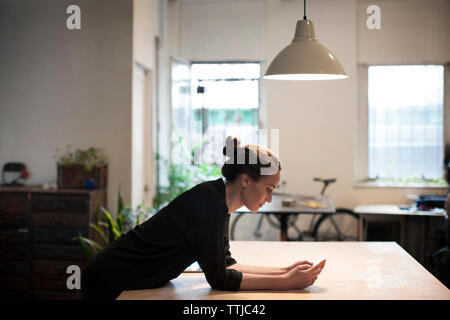 Side view of woman using smart phone while leaning on table Stock