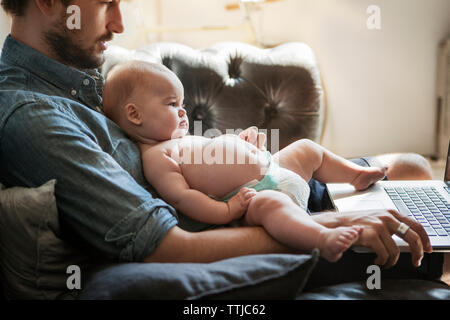 Cropped image of man using laptop computer while sitting with son at home Stock Photo