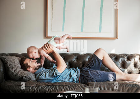 Side view of father lifting son while lying on sofa at home Stock Photo