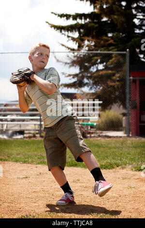 Boy throwing ball while standing at base ball field Stock Photo