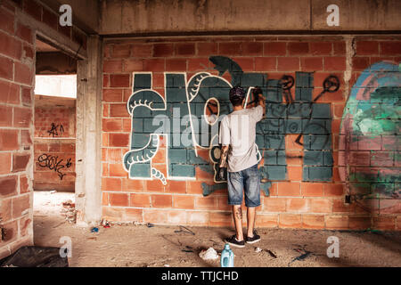 Rear view of man spraying graffiti on brick wall Stock Photo