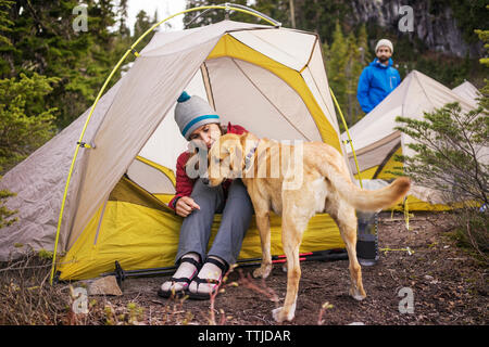 Woman with dog sitting in tent while man standing at field Stock Photo