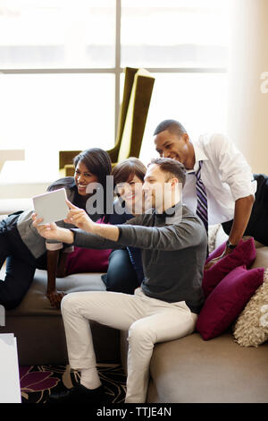 Cheerful colleagues taking selfie while sitting on sofa in office Stock Photo