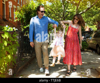 Parents holding daughters hands while walking on footpath in city Stock Photo