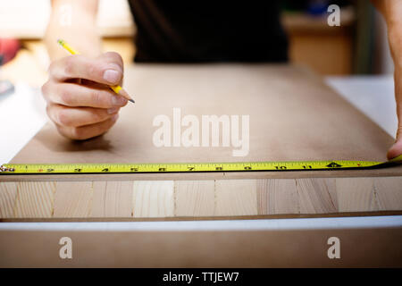 Midsection man measuring wood while working in workshop Stock Photo