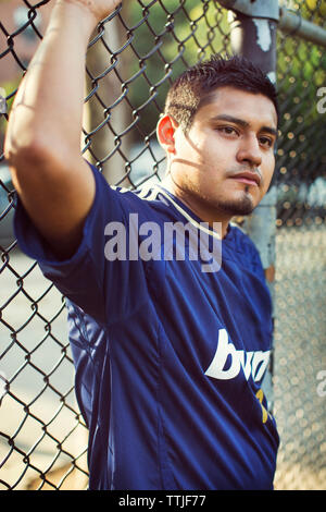 Soccer player looking away while leaning on fence at field Stock Photo