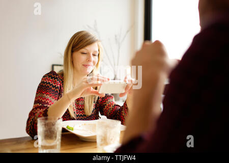Woman using mobile phone while sitting by man at dining table in home Stock Photo