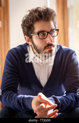 Thoughtful man looking away while sitting at home Stock Photo