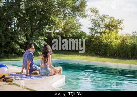Couple talking while sitting at poolside Stock Photo