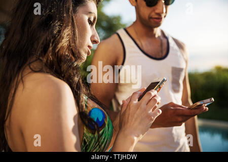 Couple using mobile phone while standing at poolside Stock Photo