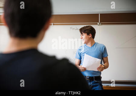 Man holding paper while standing against whiteboard in classroom Stock Photo