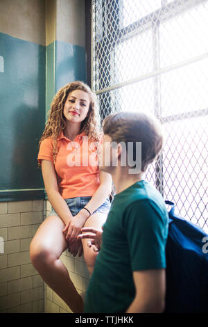 Woman sitting on window sill looking at man standing in corridor Stock Photo