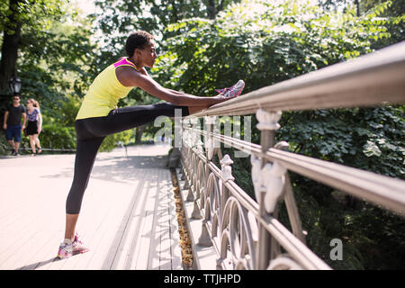 Woman practicing stretching exercise by railing at park Stock Photo