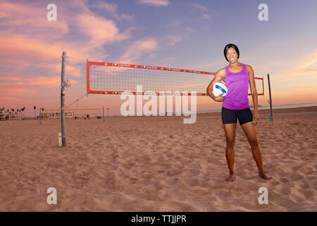 Portrait of woman holding volleyball while standing at beach Stock Photo
