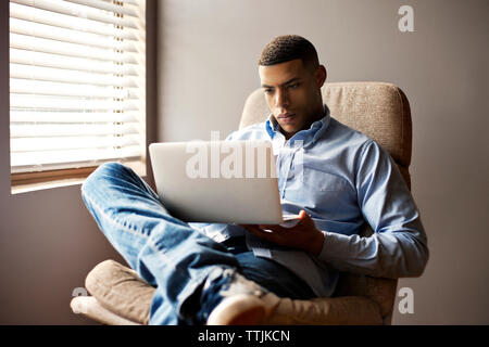 Man using laptop computer while sitting on chair at home Stock Photo