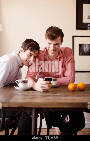 Gay couple using smart phone while sitting by table at home Stock Photo