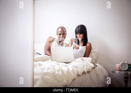 Couple looking at laptop computer while sitting on bed Stock Photo