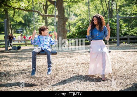 Mother and son looking at each other while playing swing in park Stock Photo