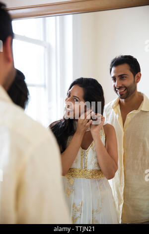 Man looking at woman wearing earring while standing in front of mirror