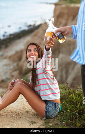 Couple toasting beer bottles while relaxing on field Stock Photo