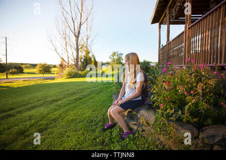 Thoughtful schoolgirl sitting on stones at yard Stock Photo