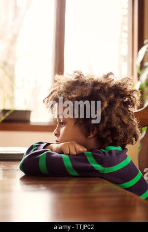 Side view of sad boy leaning on wooden table at home Stock Photo