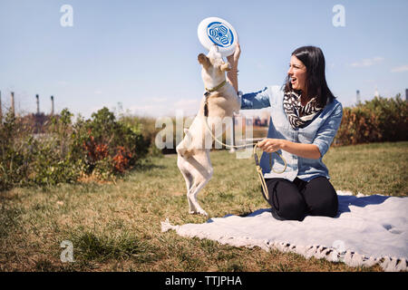 Woman giving frisbee to playful dog at park against sky Stock Photo