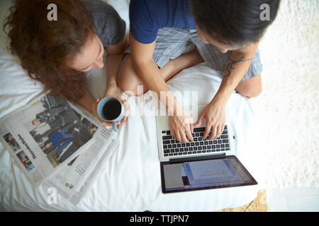 Woman having coffee while lying by man using laptop computer on bed Stock Photo