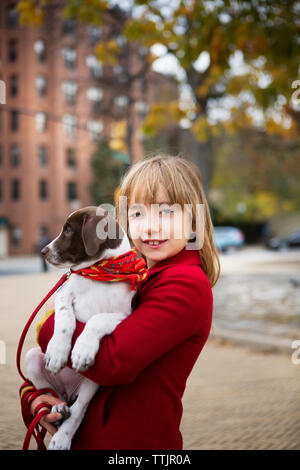 Portrait of smiling girl carrying dog while standing on footpath Stock Photo