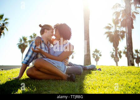 Happy couple talking while sitting on field against sky Stock Photo