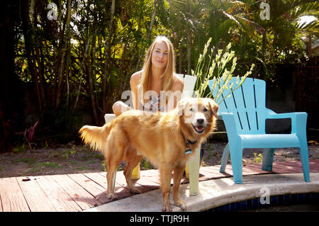 Portrait of woman with golden retriever sitting on chair at poolside Stock Photo