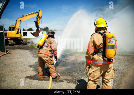 Firefighters spraying water to stop fire on sunny day Stock Photo