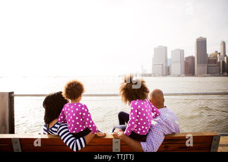 Family looking at river while sitting on bench on promenade during sunny day Stock Photo