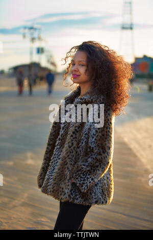 Smiling woman with curly hair wearing fur coat while standing at Coney Island Stock Photo