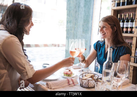 Women toasting wineglasses while sitting in restaurant Stock Photo