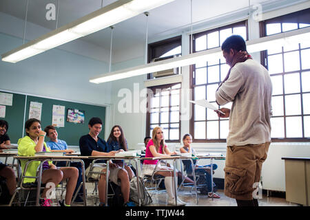 Students looking at teenage boy reading notes in classroom Stock Photo